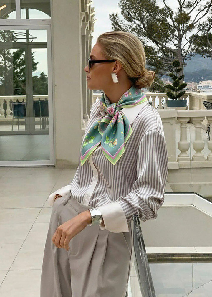 Frau im gestreiften Hemd mit Seidenschal von Feinblatt in Mintgrün mit Blumen und Schmetterlingsprint, moderner Look.