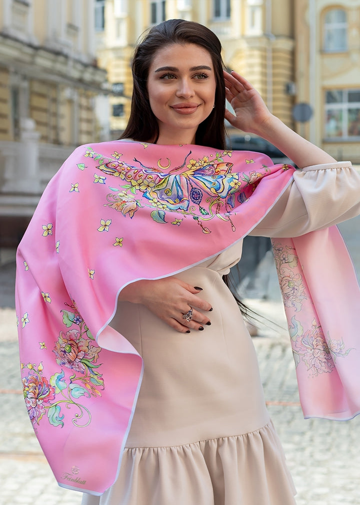 Frau trägt den Designer-Seidenschal Geschenk fuer Frauen Seidenschal Schmetterling in Rosa  luxuriöser Seidenschal mit Schmetterlingsmotiv und floralen Details, elegant über die Schultern gelegt, Design von Iryna Feinblatt.