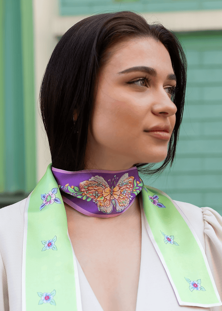 Designerschal aus reiner Seide in Lila und Mint grün mit handgemaltem Schmetterlingsmotiv, getragen als eleganter Halsschmuck von einer stilvollen Frau – luxuriöses Accessoire für Frühling und Sommer