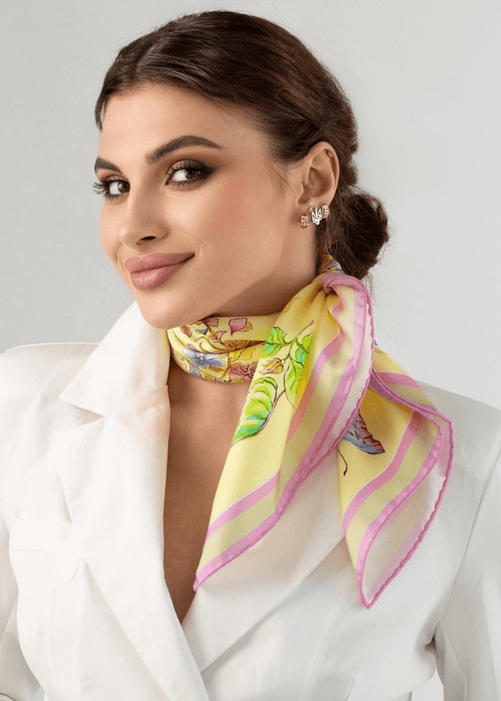 Woman wearing a yellow silk scarf with floral design, styled elegantly with a white outfit and soft makeup.