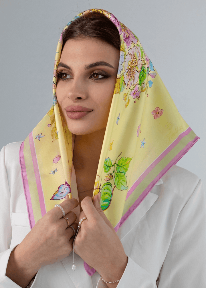 Woman wearing a yellow silk scarf with floral design, smiling, showcasing summer style and elegance.