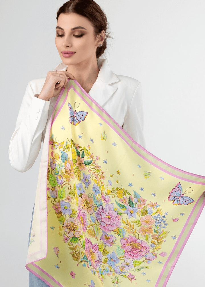 Elegant woman holding a yellow silk scarf with floral and butterfly designs, showcasing its vibrant colors and artistry.