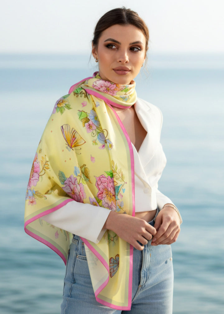 Frau trägt das Seidenkopftuch „Herz aus Blumen in Gelb“ von Iryna Feinblatt elegant um die Schultern – zarte gelbe Seide mit Blumen und Schmetterlingen