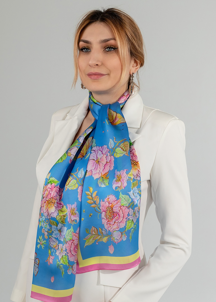 Blaues Seidentuch mit Blumenmuster um den Hals einer Frau im hellen Anzug gebunden